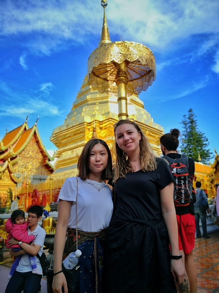 Two people smiling in front of a golden temple structure.