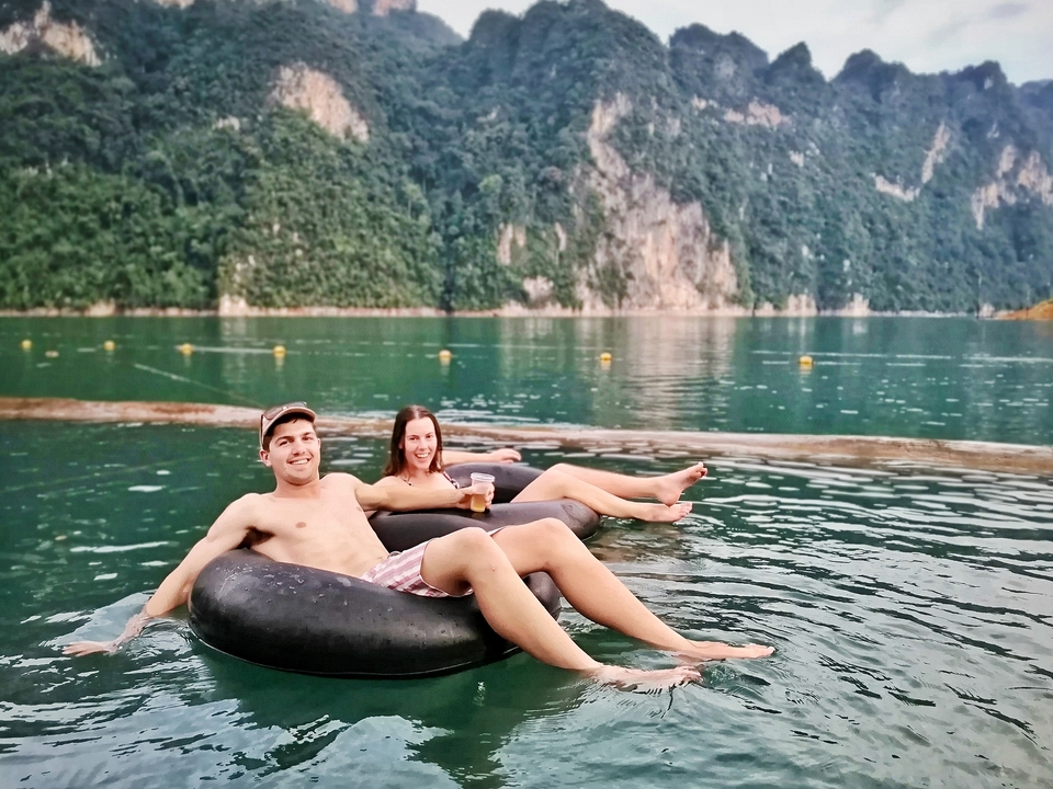 Two people floating on tubes in water with cliffs in the background.