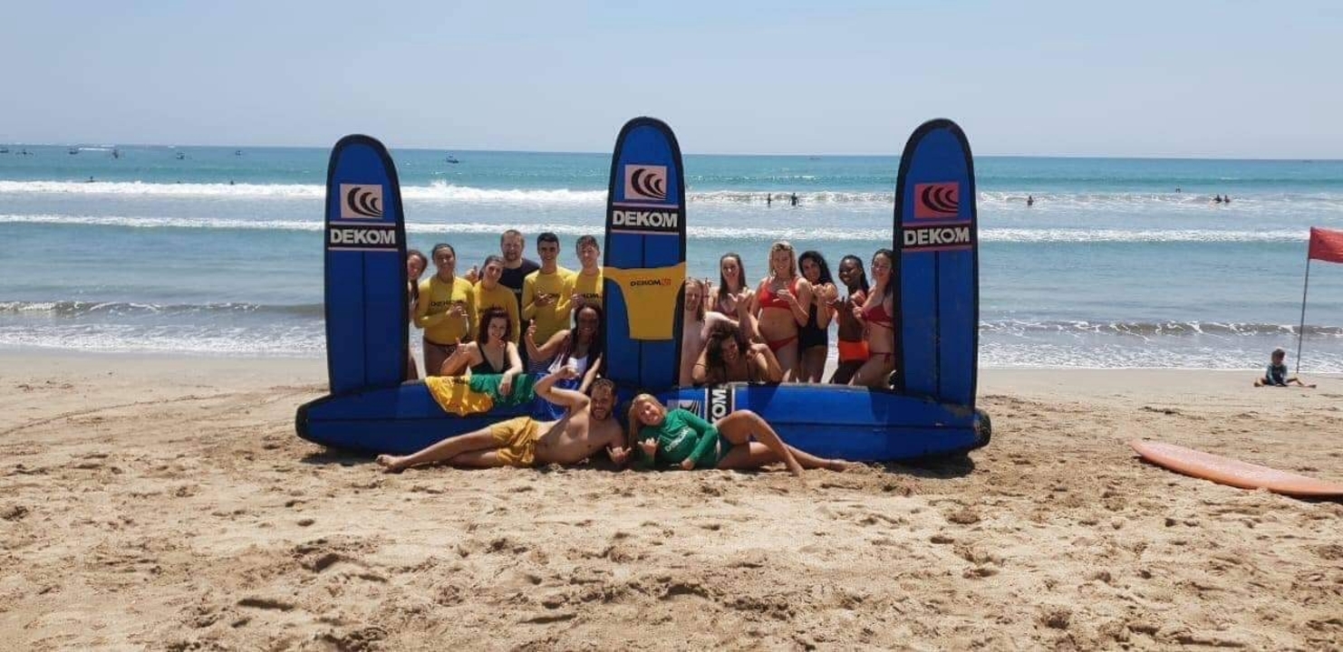 Group posing with surfboards on a beach.