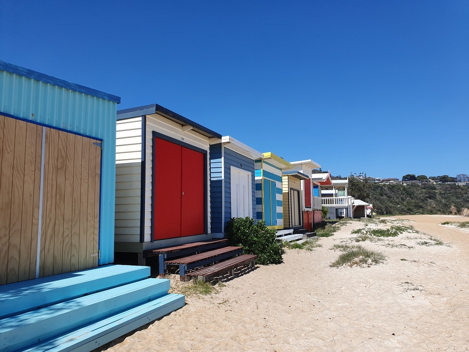 Rangée de cabines de plage colorées le long d'une rive sablonneuse.