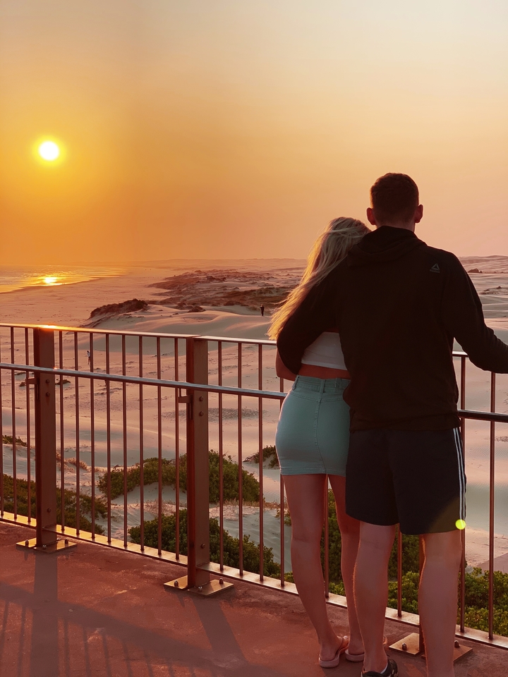 Couple embracing while watching the sunset over sand dunes.