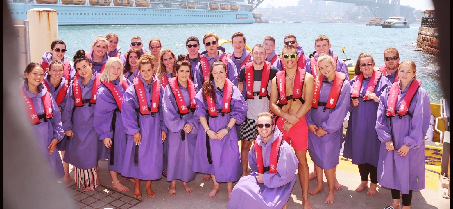 Photo de groupe de personnes portant des gilets de sauvetage avec un navire de croisière en arrière-plan.