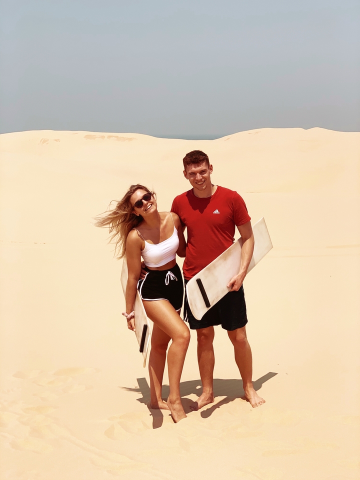 Couple posant sur les dunes de sable avec des planches.