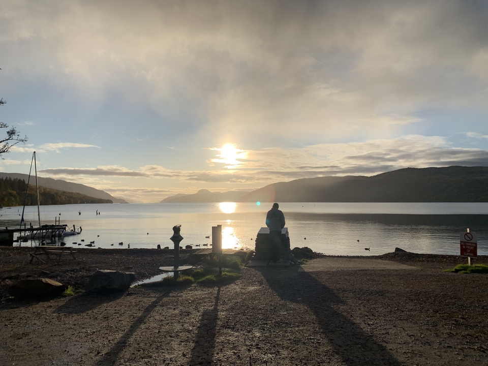 Silhouette d'une personne au bord d'un lac au coucher du soleil.