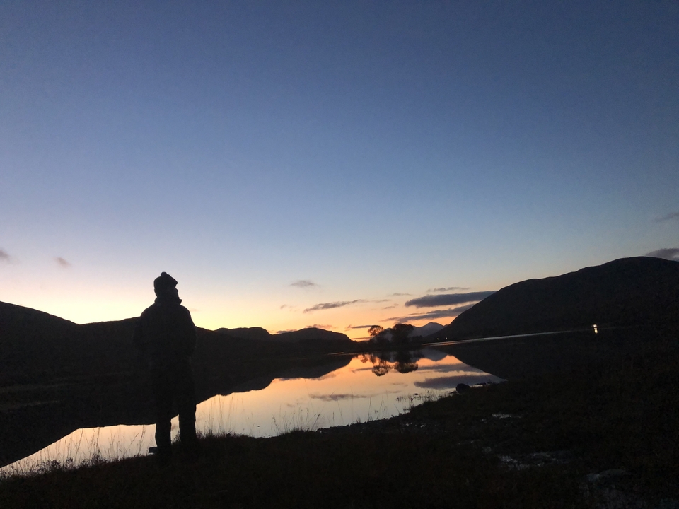 Personne en silhouette devant un lac au coucher du soleil.