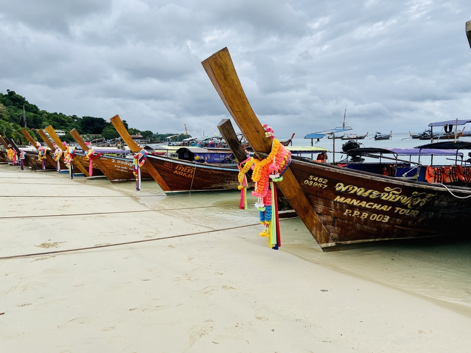 Colorful long-tail boats lined up by a beach.