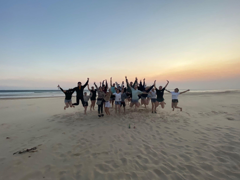 Groupe de personnes sautant sur une plage au coucher du soleil.