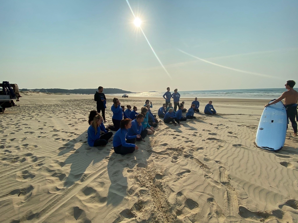 Scène de plage avec des gens assis sur le sable écoutant un moniteur de surf.