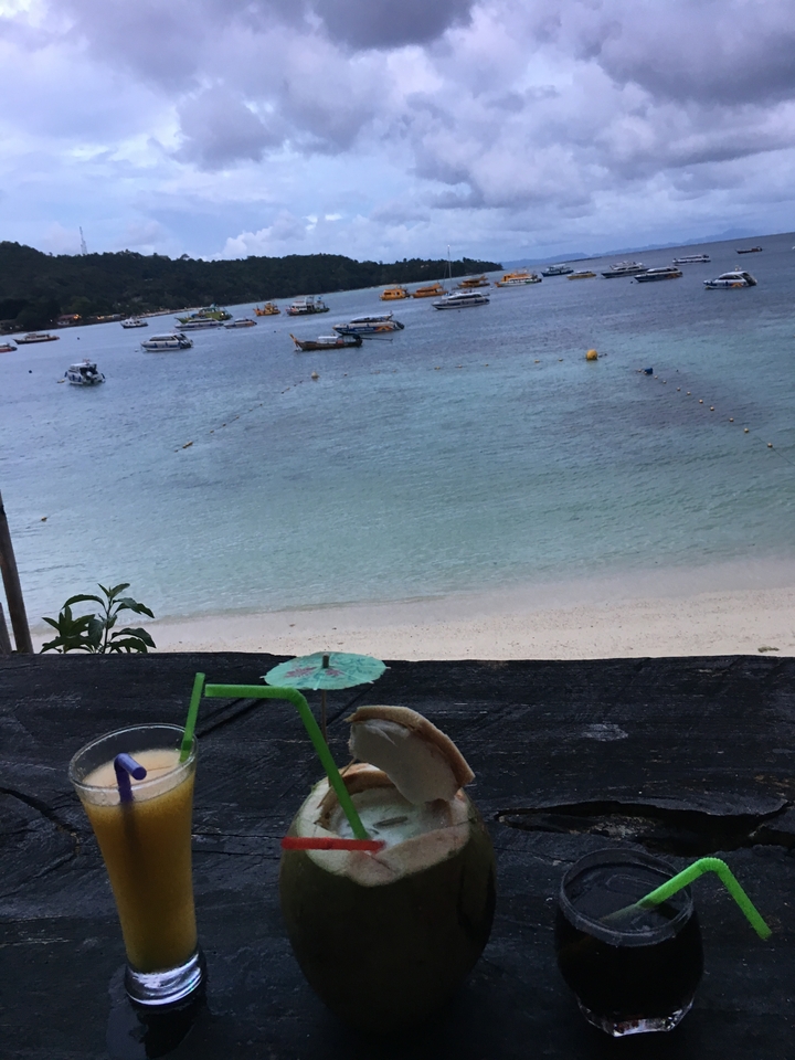 View of a beach with boats and a drink in the foreground.