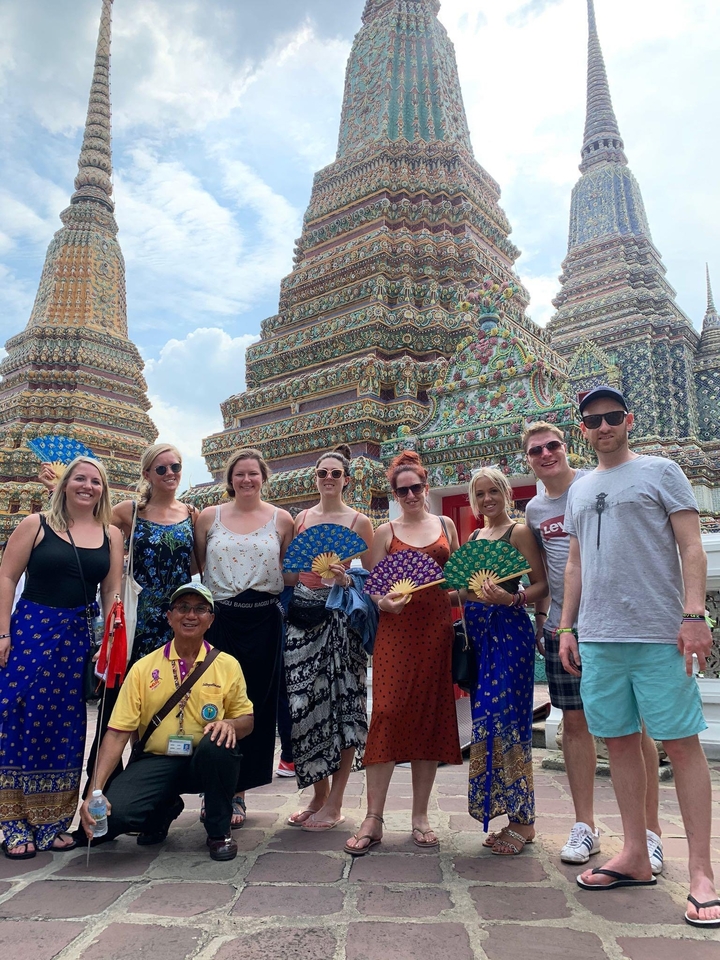 Group of people posing in front of colorful Thai temples with ornate details.