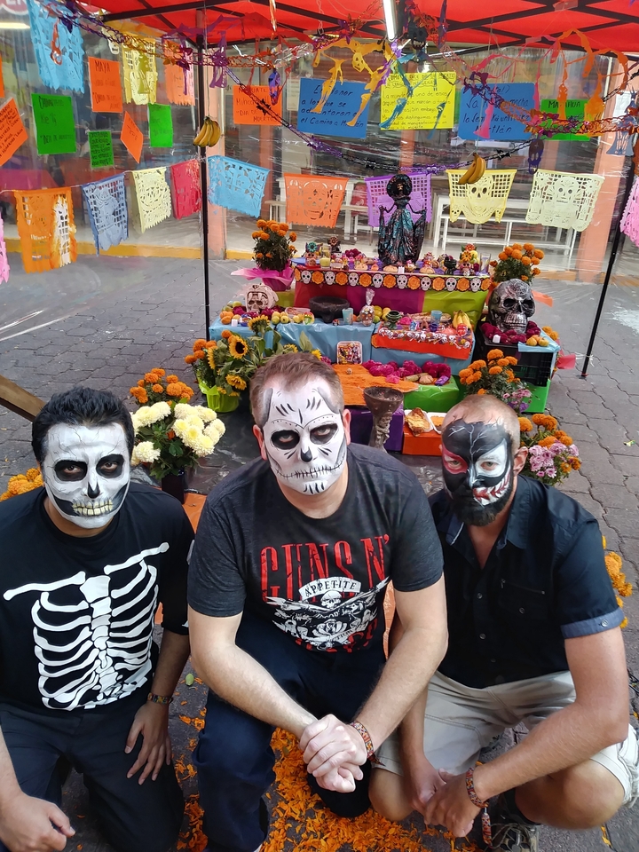 Three men with painted faces sitting by an altar.