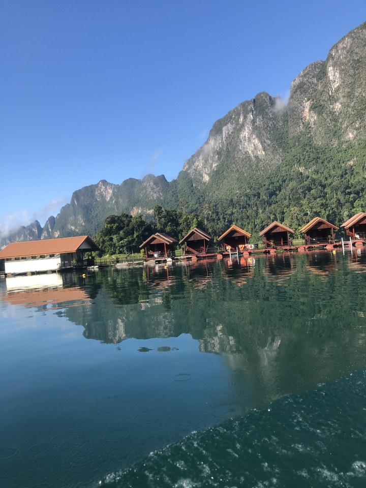Floating houses on a calm lake with mountains.