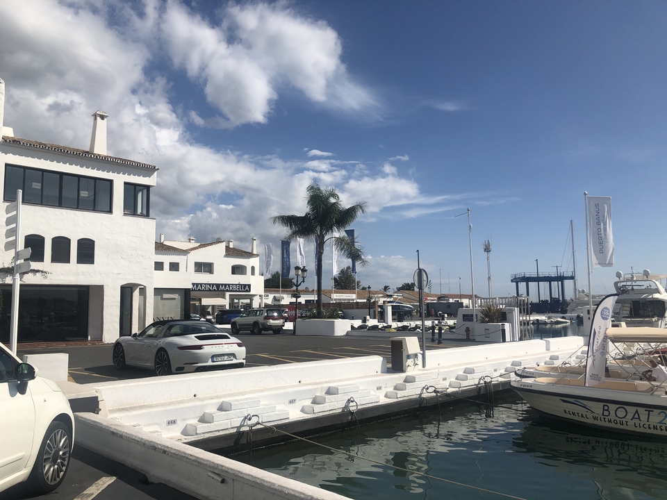 Marina with luxury cars and boats, clear sky backdrop.
