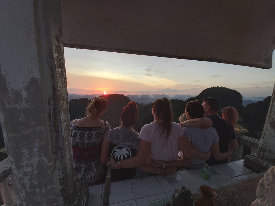 A group watching a sunset over distant cliffs from a building.