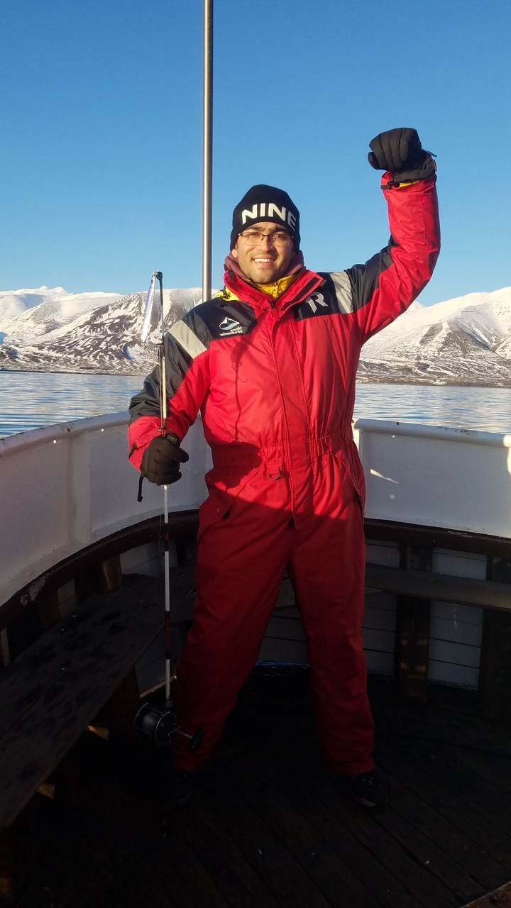 Person dressed in a red suit on a boat with snow-covered mountains in the background.