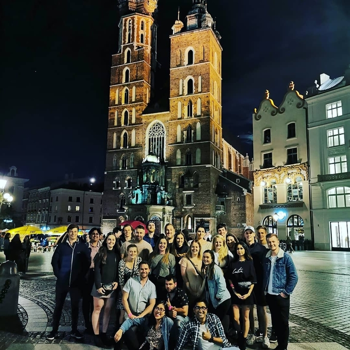 Large group posing in front of an illuminated medieval building at night.