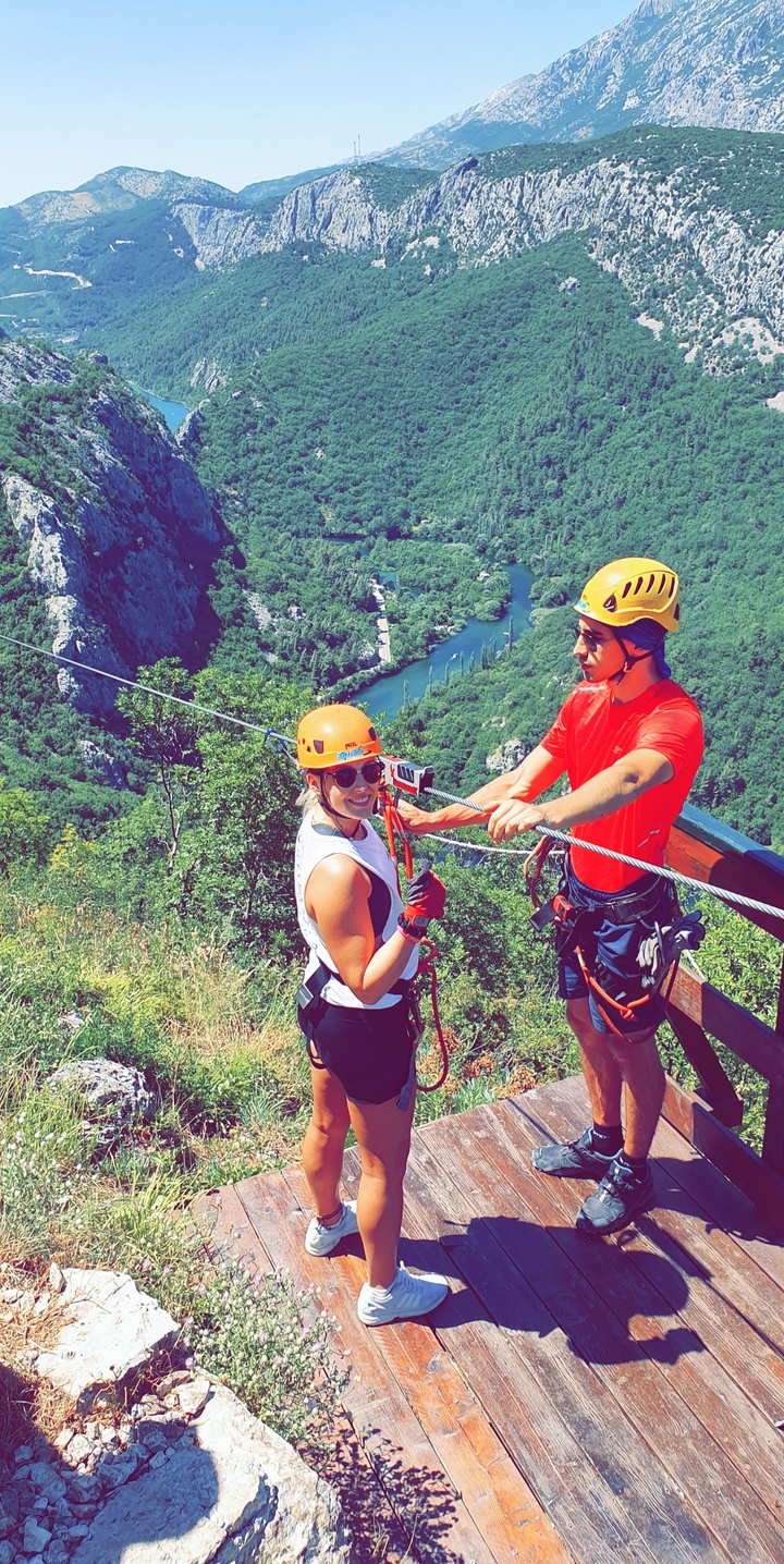 Deux personnes se préparant pour une aventure en tyrolienne au-dessus d'un paysage montagneux.