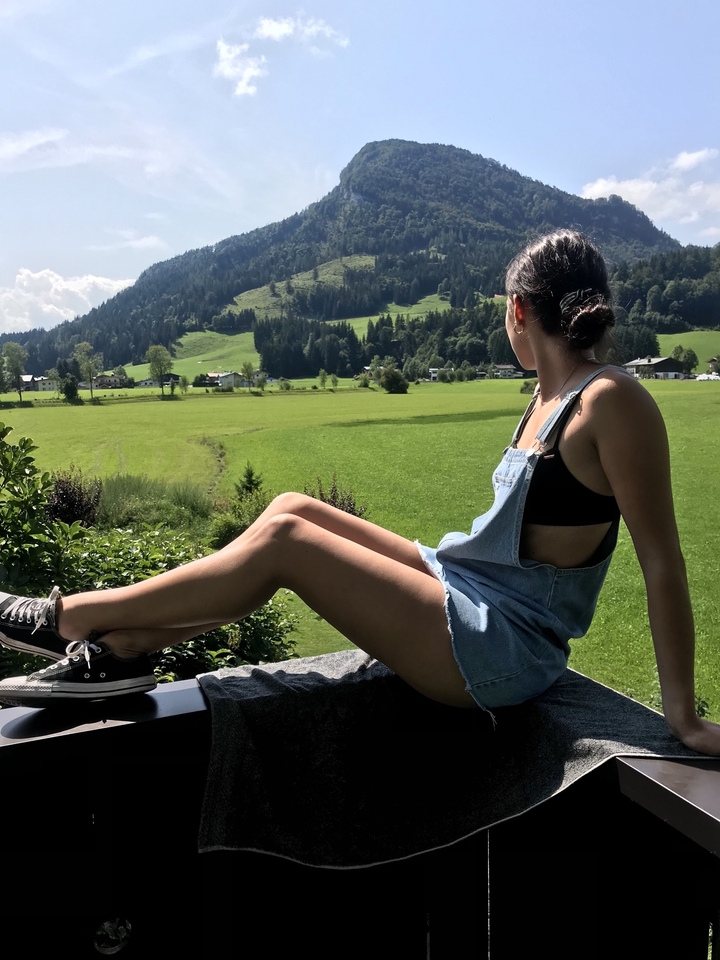 A person sitting on a stone wall with a green field and hills in the background.
