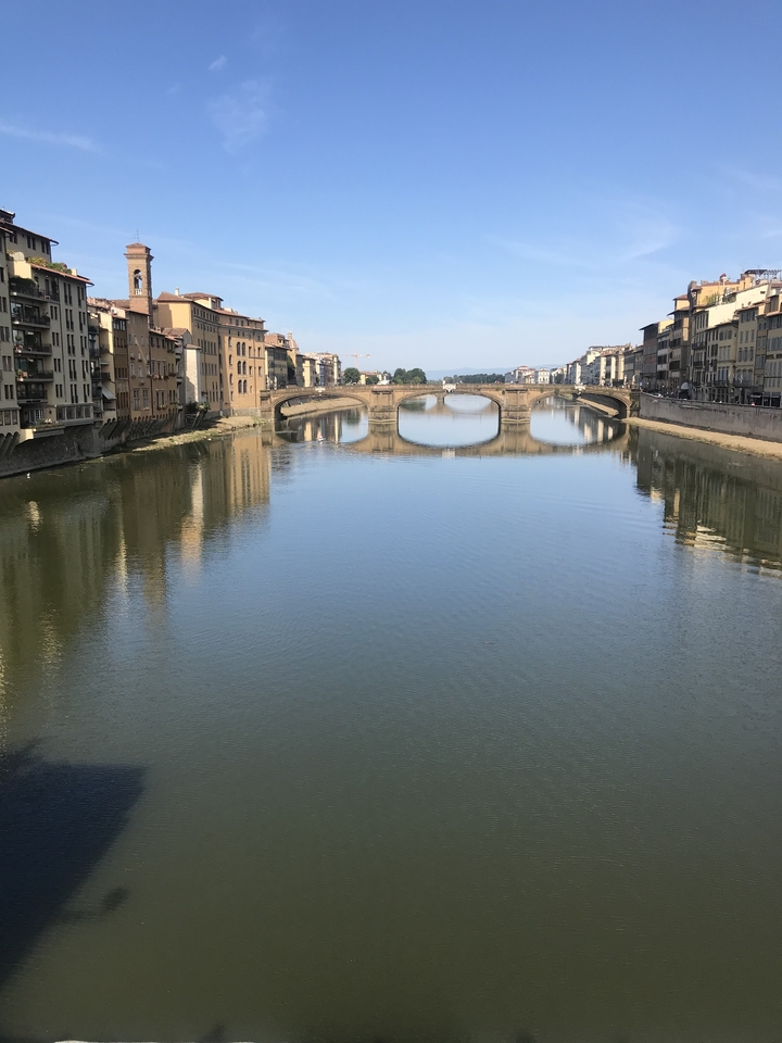 A river with an arched bridge and buildings reflecting on the water.