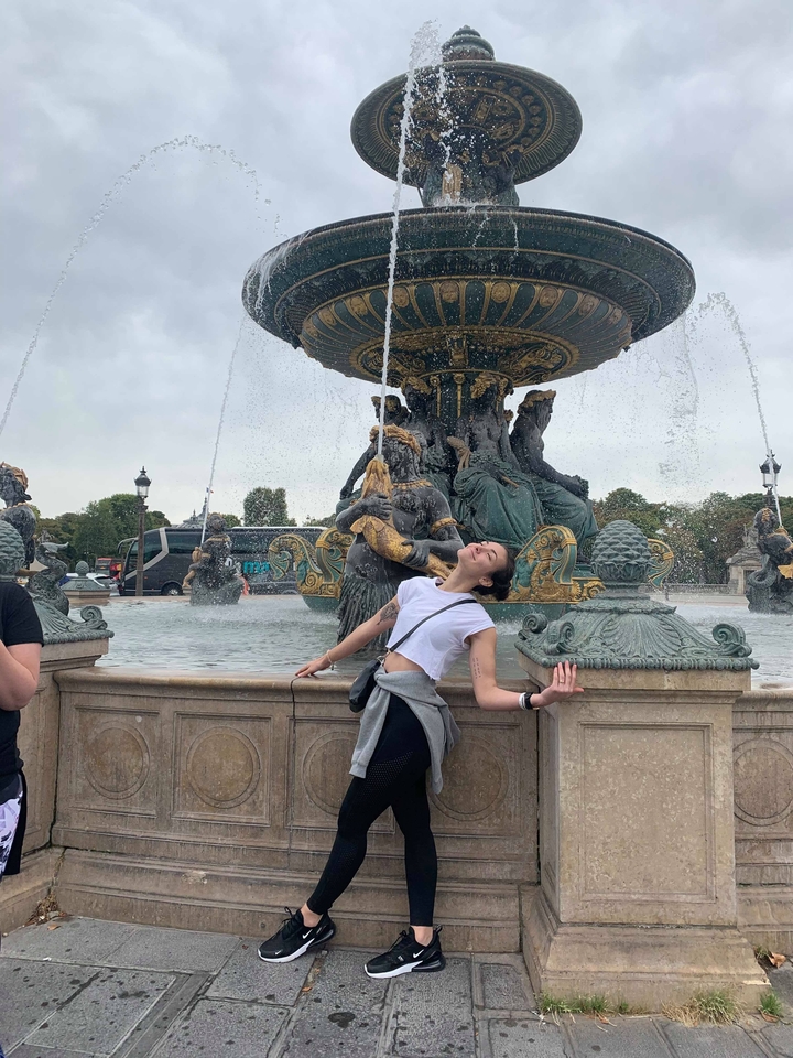 Person posing in front of a fountain with statues.