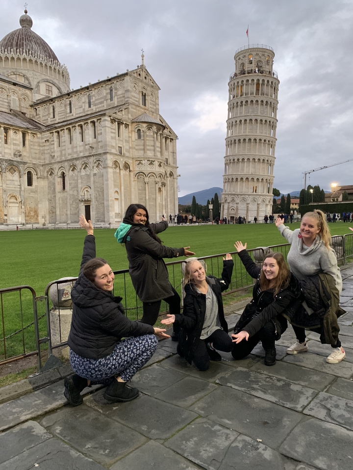 Group posing creatively in front of the Leaning Tower of Pisa.