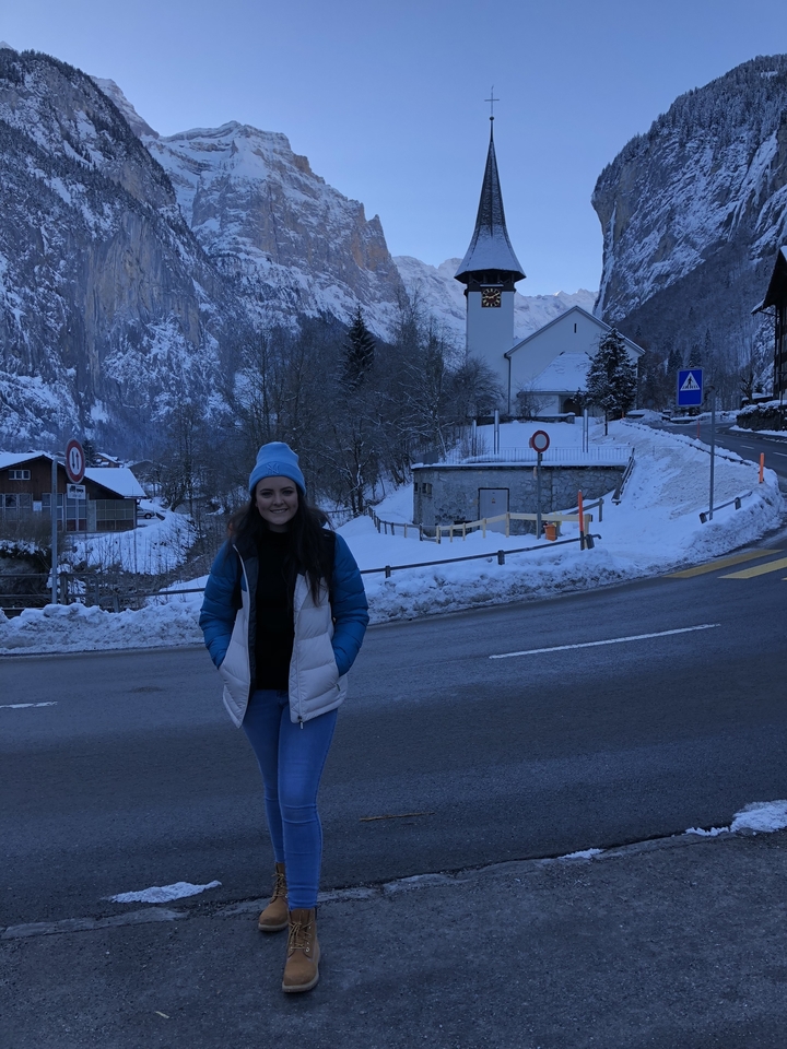 A person standing on a snowy roadside with mountains.