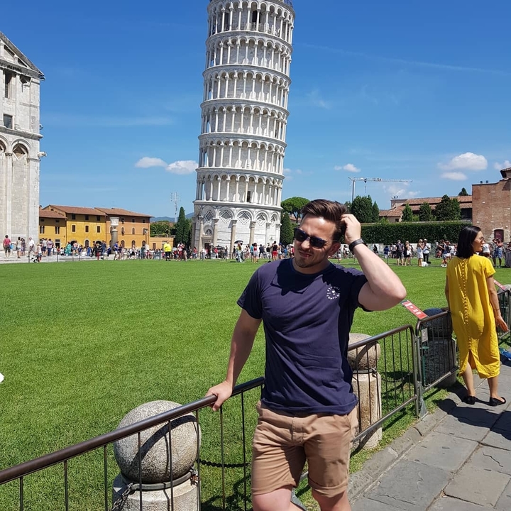 Person posing near a famous leaning tower.