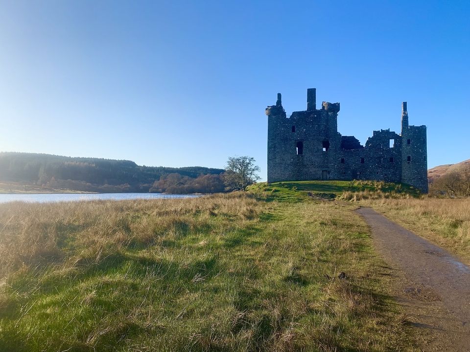 Ruins of a castle by a lake under a clear sky.