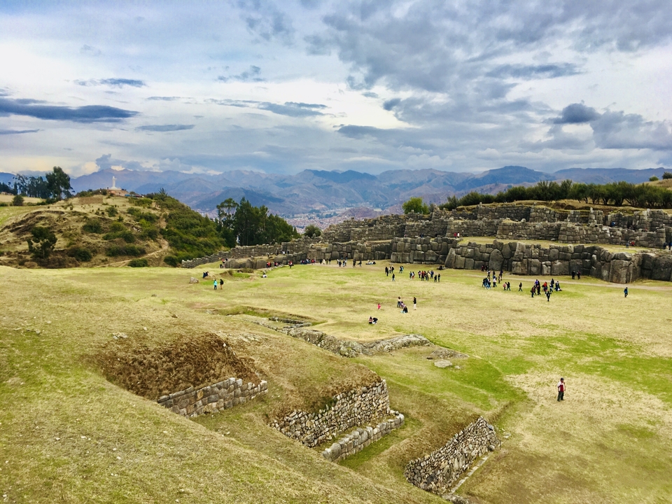 Ruines anciennes avec des personnes qui marchent et des montagnes en arrière-plan.