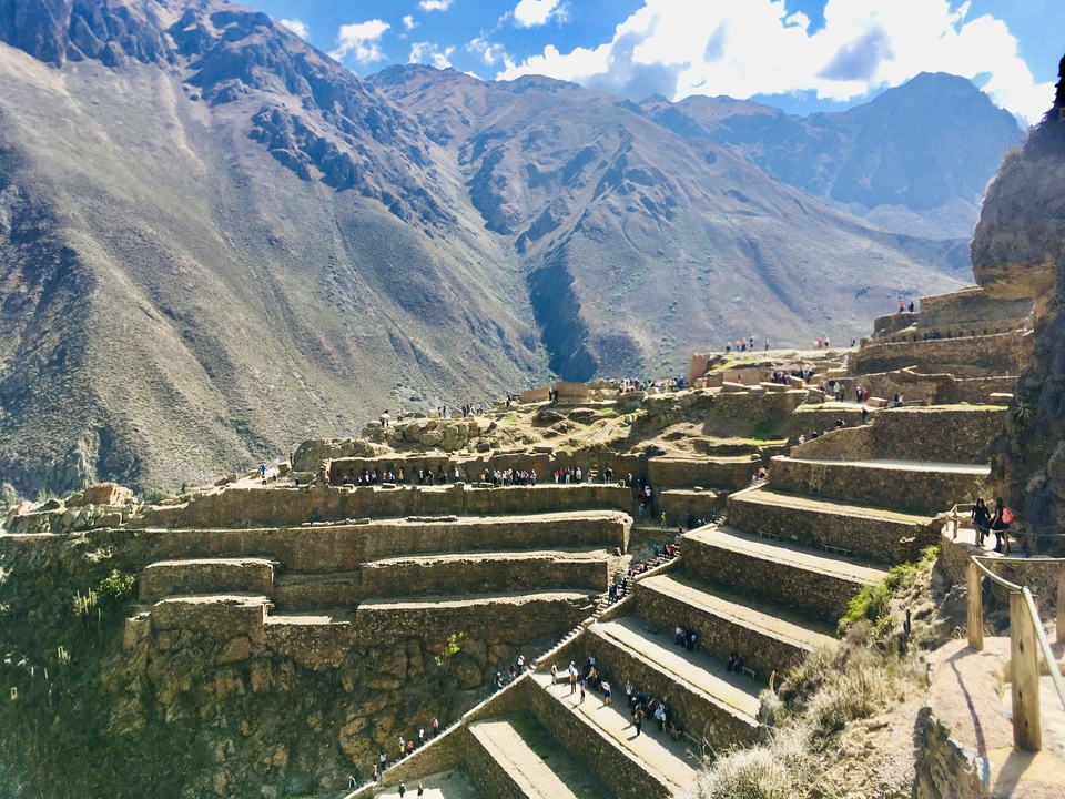 Ruines en terrasses avec des touristes et des montagnes.