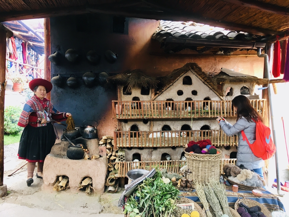 Deux personnes à côté d'un four traditionnel andin, tenant des textiles.