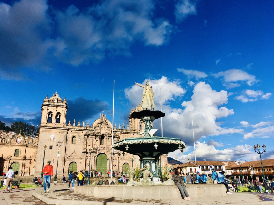 Fontaine devant une cathédrale sous un ciel bleu lumineux avec des nuages.