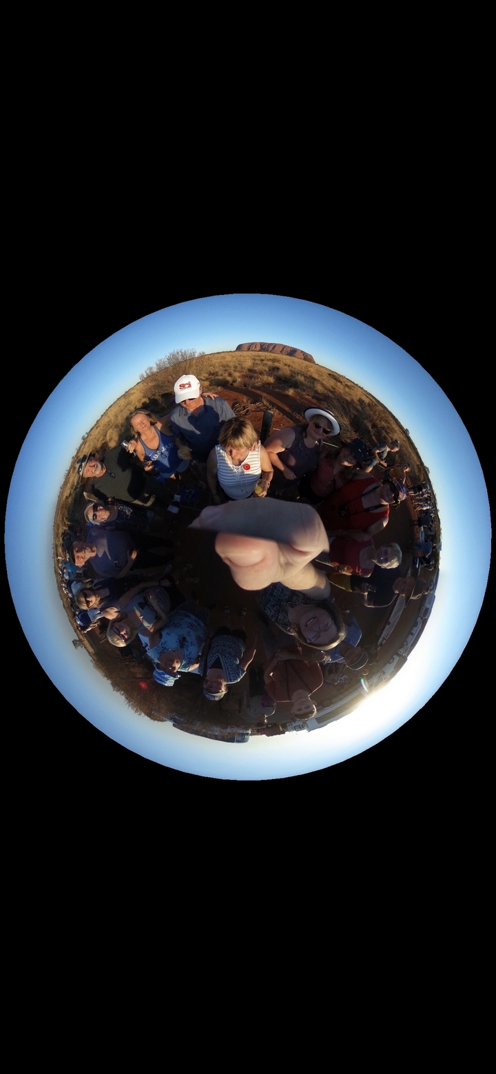 Groupe de personnes debout en cercle autour de la caméra à l'extérieur.