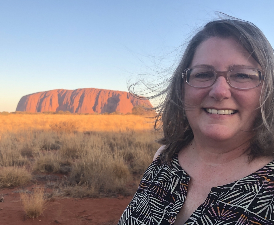 Femme souriante avec la formation rocheuse d'Uluru en arrière-plan.