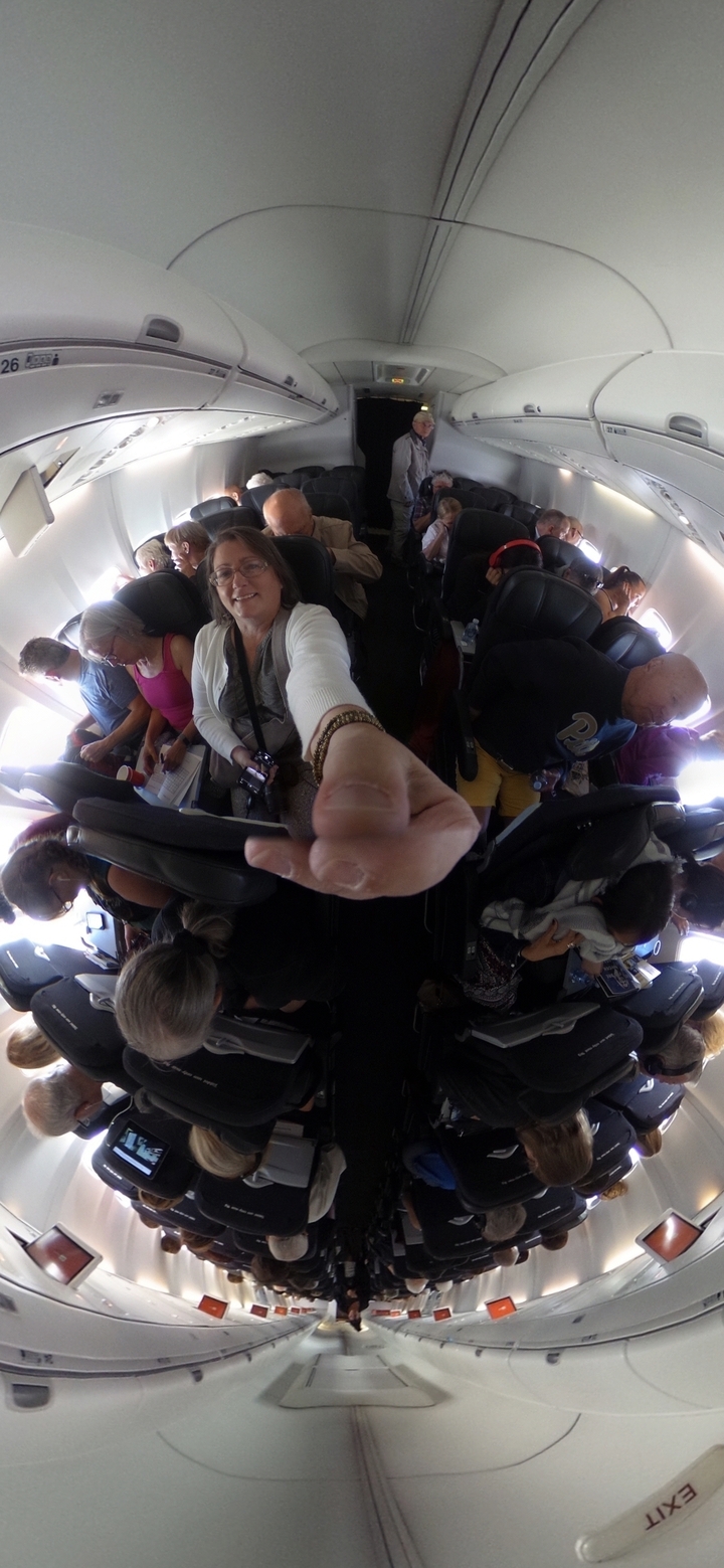 Personne prenant un selfie dans un avion avec d'autres passagers visibles.