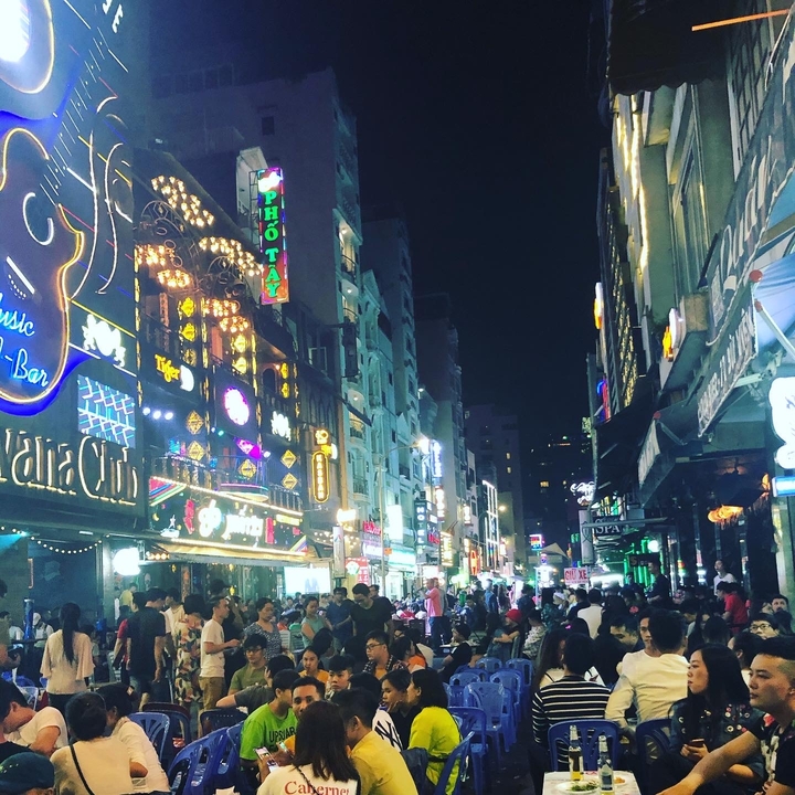 A busy street at night with bright neon signs and a bustling crowd.