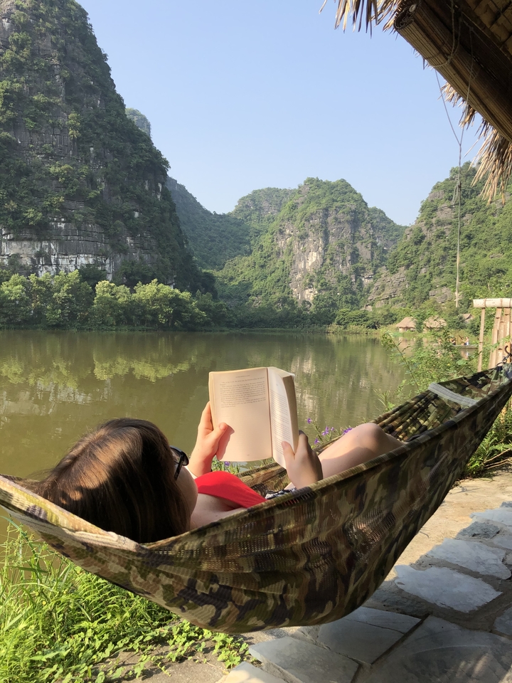 Person relaxing on a hammock reading a book by a peaceful lake.