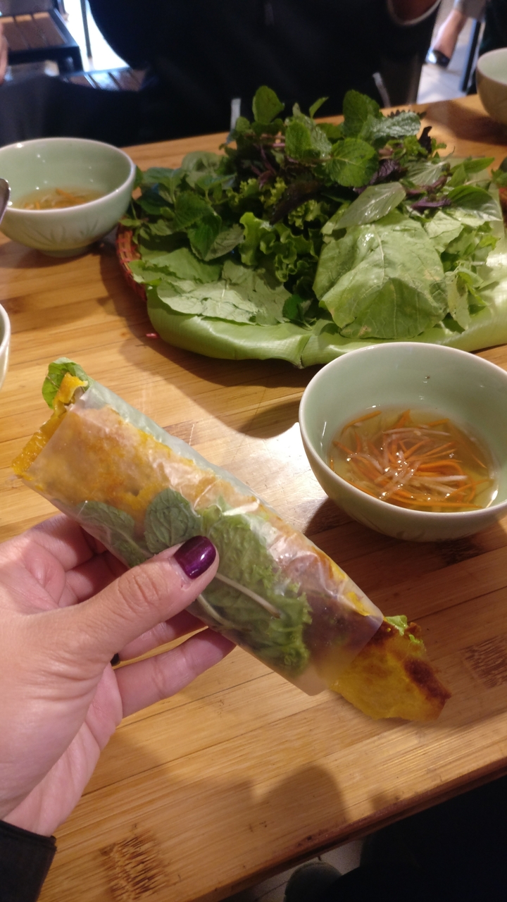 Une main tenant un rouleau de printemps avec un bol de sauce à tremper à proximité.