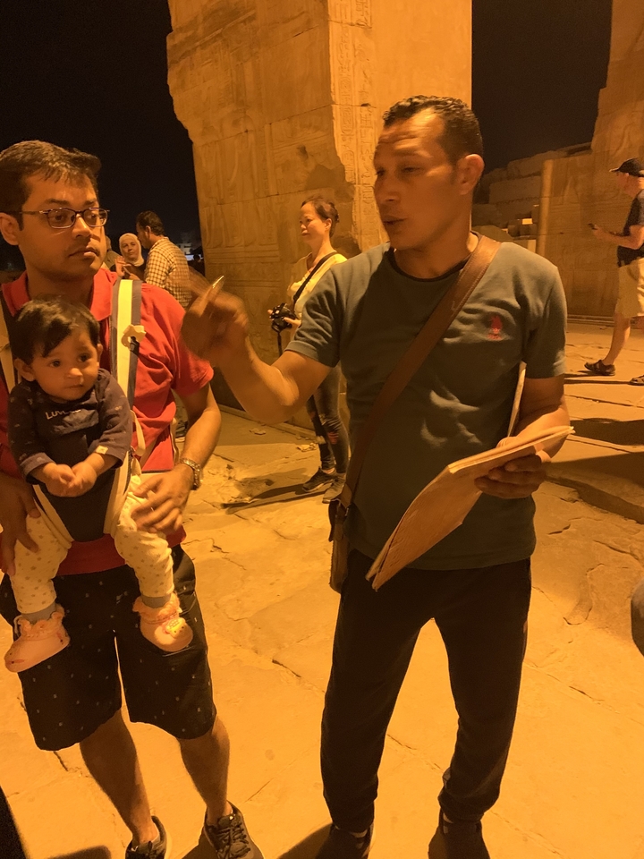 Deux personnes la nuit, l'une tenant un enfant et l'autre faisant des gestes avec un carnet.