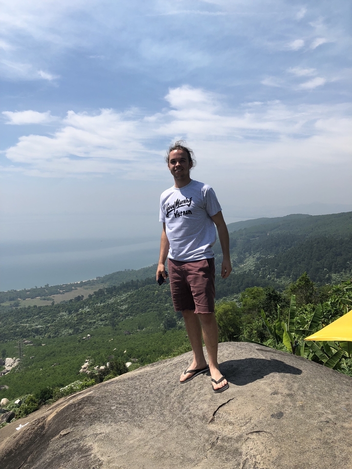 Person posing on a hill with a scenic view of the coastline.