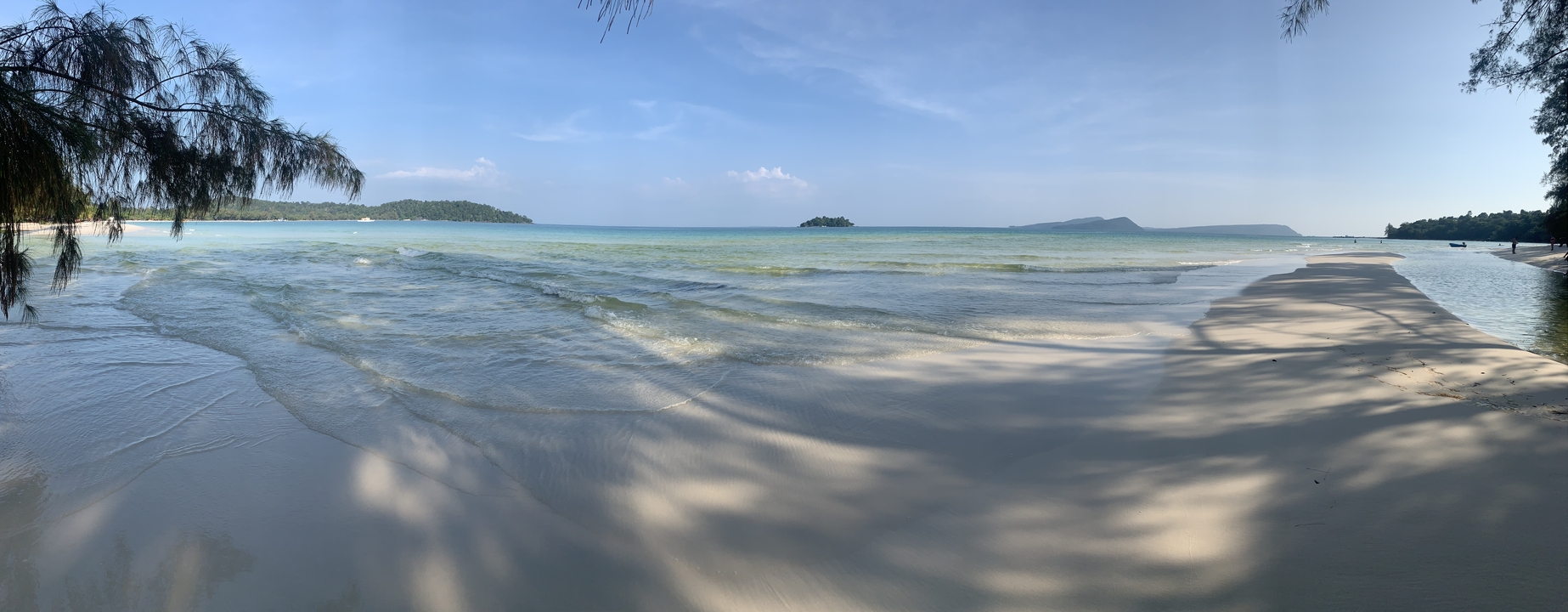 Tranquil beach scene with clear shallow waters and distant islands.