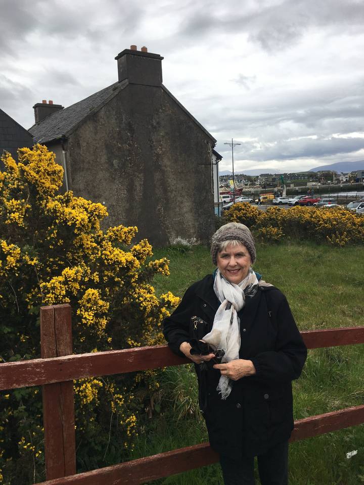 Femme debout à côté d'une clôture avec des fleurs et une maison.