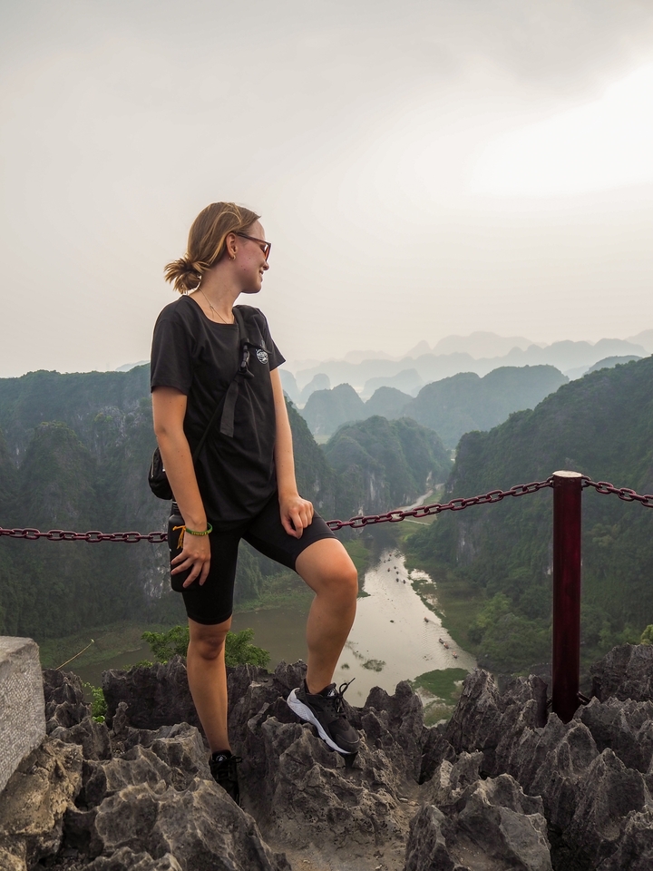 Person standing at a viewpoint overlooking lush green mountains.
