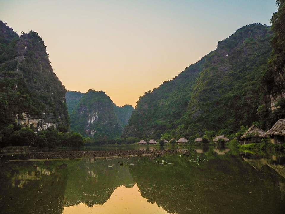 Serene lake surrounded by lush green cliffs at sunset.