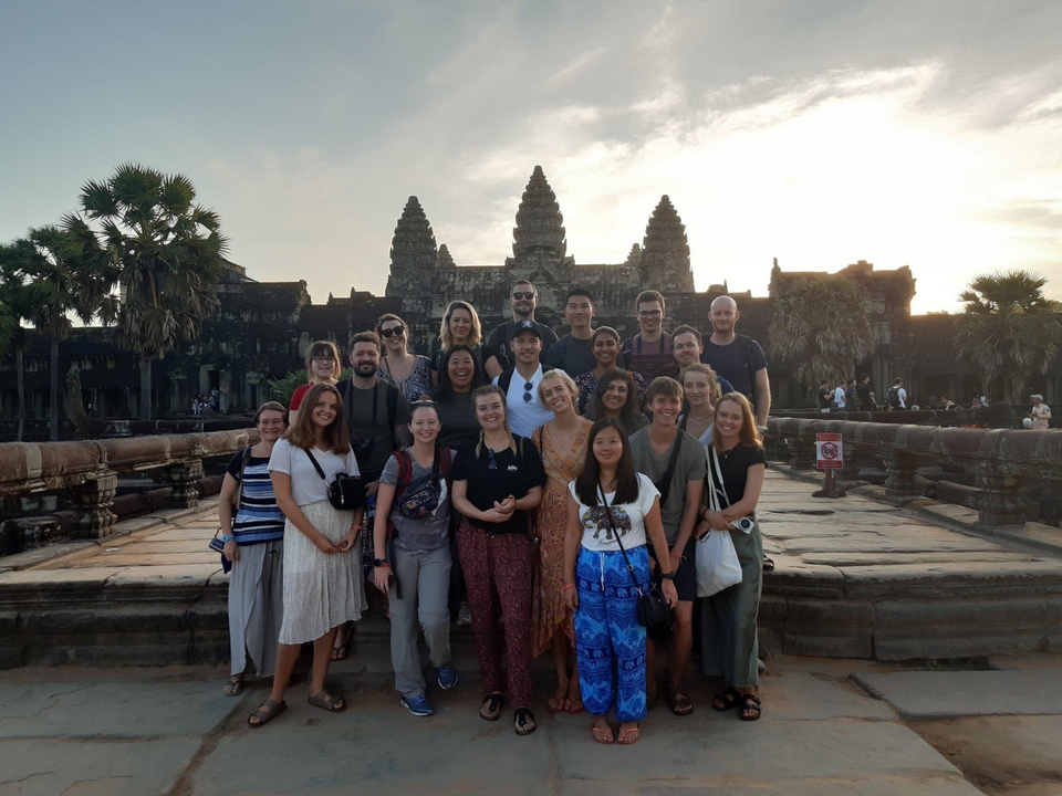 Group of tourists posing in front of an ancient temple at sunset.