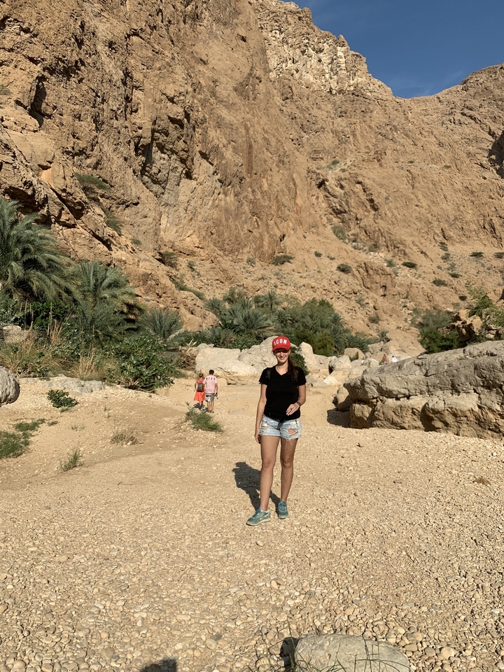 Woman standing in a rocky landscape with palm trees.