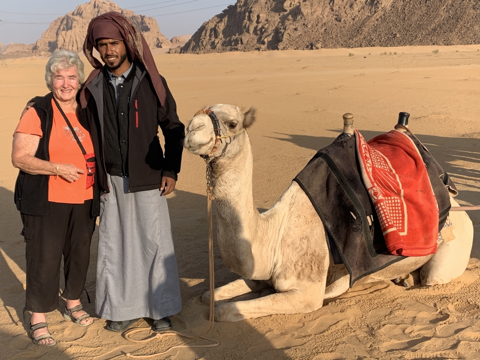 Person standing beside a camel in a desert landscape.