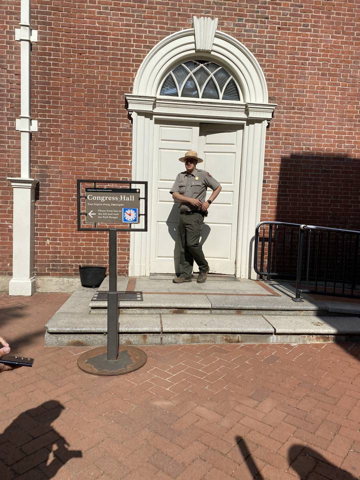 "Garde forestier debout près d'un bâtiment historique."

Note: Depending on the context, "park ranger" could also be translated as "garde de parc" (for a general park ranger) or "agent des parcs" (more formal).
