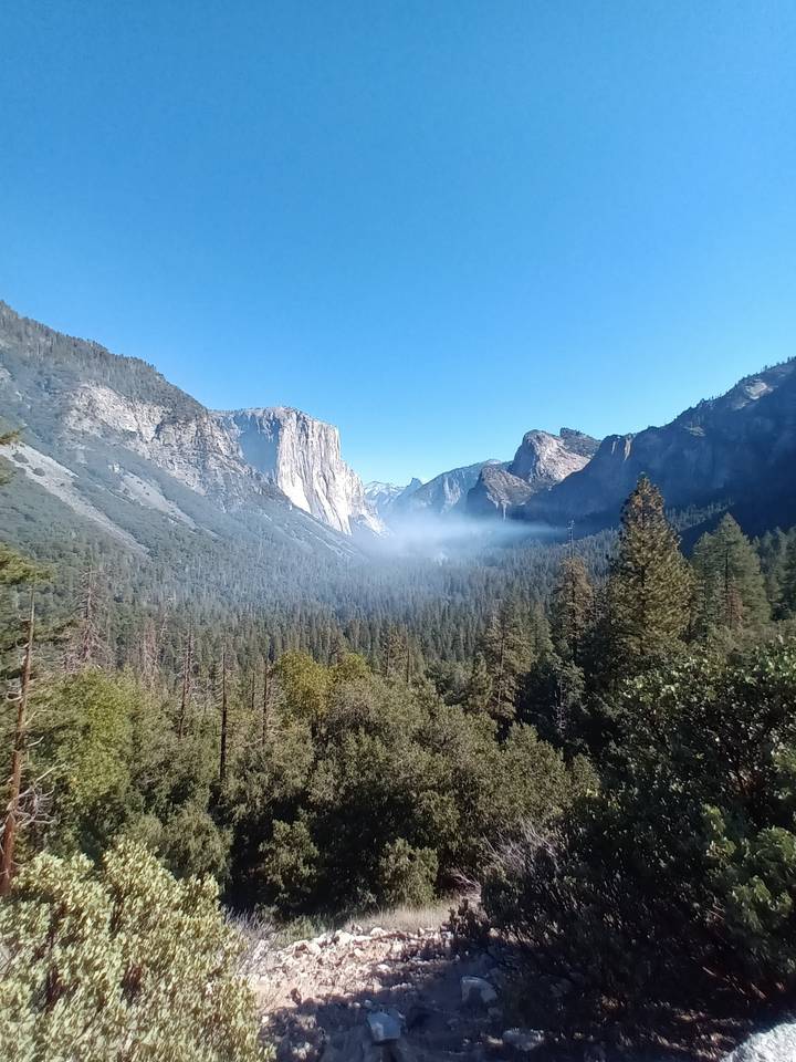 Vue dramatique d'une vallée embrumée entourée de montagnes.