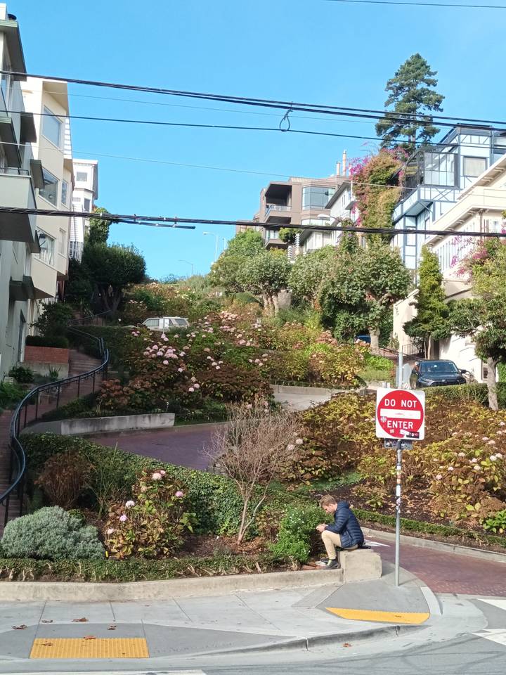 Rue courbe dans une ville, présentant une pente raide et un panneau Sens interdit.